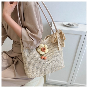 Détail d'un cabas tressé en paille avec fleurs en tissu décoratives et nœud en dentelle