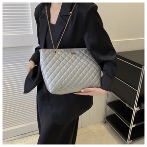 Close-up of silver-gray quilted tote bag with gold chain strap worn by a model