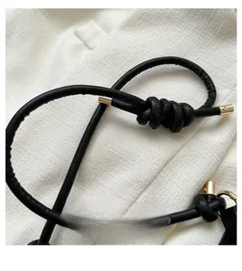 Detail of black leather knotted strap with gold metallic tips on textured fabric