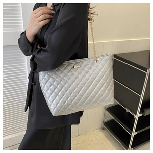 Detail of silver quilted tote bag with golden chain strap on a model shoulder