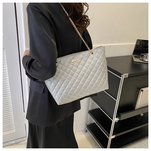 Detail of silver quilted tote bag featuring gold chain strap and elegant metal plaque