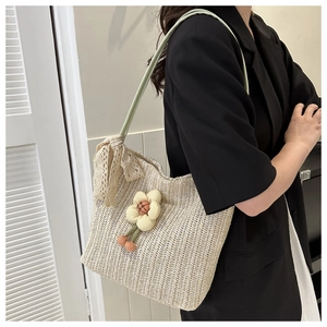 Détail du sac en paille avec breloque fleurie et bandoulière verte sur mannequin
