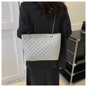 Close-up of silver quilted tote bag with gold chain strap on model in black blazer
