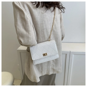 Detail of white quilted crossbody bag with gold chain strap and metallic twist lock