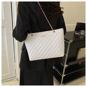 Detailed view of white quilted tote bag with gold chain strap worn with black blazer