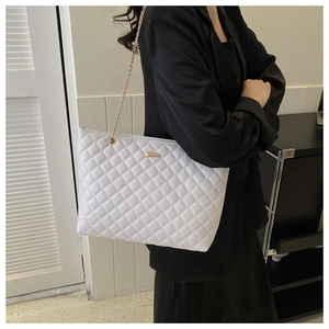 Close-up of white quilted tote bag with gold chain strap worn over black blazer