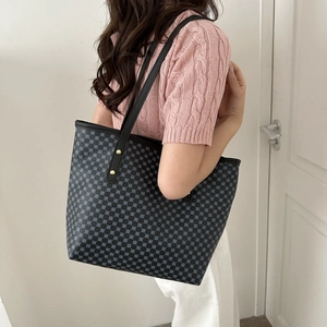 Chic monogram tote bag with blue patterns and leather straps shown on a model