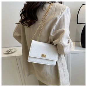 Close-up of ivory quilted chain bag with gold metal lock on a model in minimalist setting