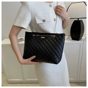 Detailed view of black quilted chain shoulder bag worn with elegant dress