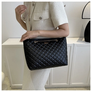Close-up of black quilted shoulder bag with gold chain and metal lock detail