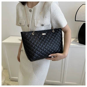 Detail of black quilted leather shoulder bag with gold chain strap on a model