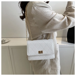Detail of white quilted crossbody bag with gold twist lock and chain strap on shoulder