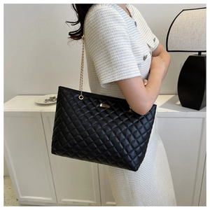 Detail of black quilted shoulder bag with golden chain strap and metallic buckle