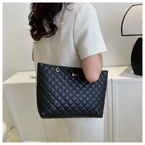 Close-up of black quilted tote bag with gold chain strap worn on person's shoulder