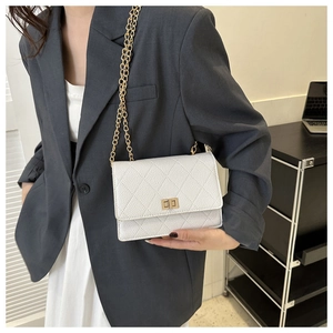 Detail of white quilted crossbody bag with golden chain strap on gray blazer outfit