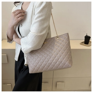 Quilted light brown tote bag with gold chain strap shown on a model in a minimal setting