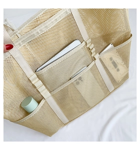 Detailed view of beige mesh tote bag with front pockets holding a tablet and phone