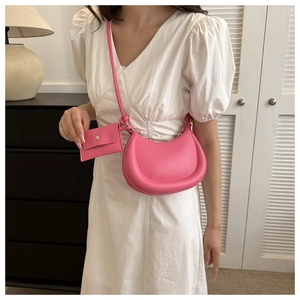 Pink crescent shoulder bag with matching coin purse and gold hardware on white dress