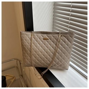 Detail shot of beige quilted faux leather tote bag with gold chain and metal plaque