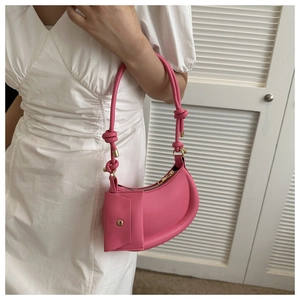 Detail of pink half-moon shoulder bag with knot strap and small pouch worn by model