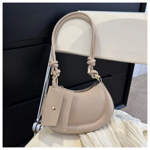 Detail of beige crescent shoulder bag with knot handle and detachable mini pouch on chair