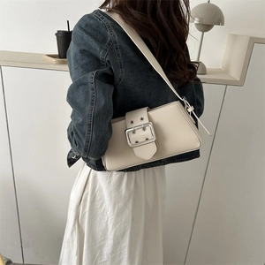 Minimalist beige shoulder bag with large silver buckle shown on a model in a casual setting
