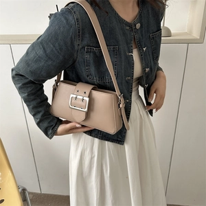 Chic beige underarm bag with oversized silver buckle on a stylish model in denim outfit