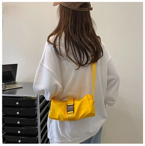 Detail shot of bright yellow nylon crossbody bag with black buckle worn by a model