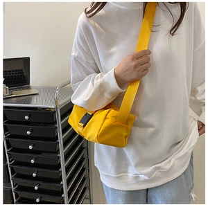 Detail of bright yellow nylon crossbody bag with black plastic buckle and adjustable strap