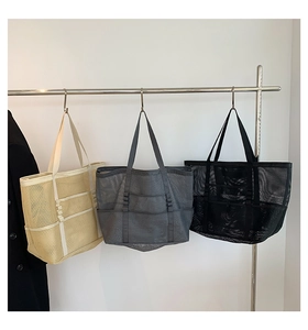 Three mesh beach bags in beige, grey, and black colors hanging on metal hooks for display