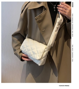Sac bandoulière blanc matelassé avec large sangle, porté par un mannequin en trench-coat
