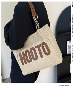 Détail du sac cabas en toile beige avec lettrage HOOTO marron et bandoulière chaîne