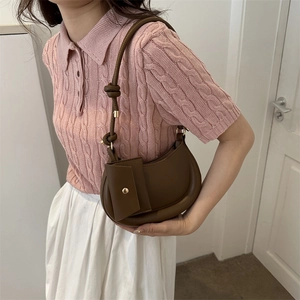 Brown crescent shoulder bag with knot detail and small pouch on pink knit sweater