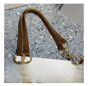 Détail macro de la bandoulière en cuir marron et du connecteur en anneau métallique doré