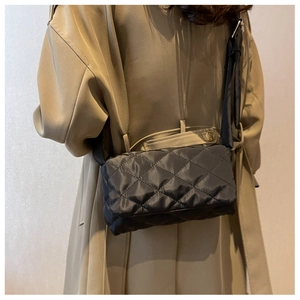 Détail d'un sac bandoulière en nylon noir matelassé avec motifs à losanges sur un trench-coat