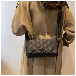 Détail d'un sac bandoulière en nylon noir matelassé porté avec un trench-coat kaki