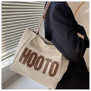 Détail d'un sac cabas beige avec lettres en cuir et bandoulière en chaîne dorée
