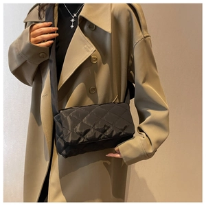 Détail d'un sac bandoulière en nylon noir matelassé porté avec un trench-coat classique