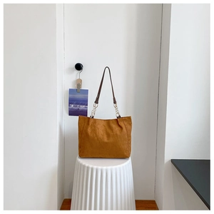 Sac cabas en daim marron avec bandoulière chaîne sur un socle décoratif blanc