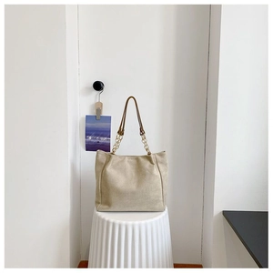 Détail du grand sac cabas en daim beige avec bandoulière chaîne sur fond blanc pur