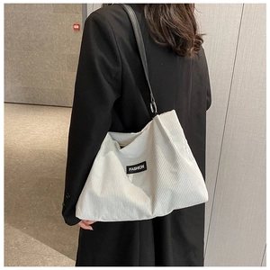 Detail of corduroy tote bag featuring a 'FASHION' label and black leather shoulder strap