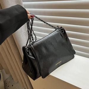 Detail of glossy pleated leather texture and silver chain strap on a black tote bag