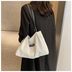 Detail of white corduroy tote bag featuring fashion label and black leather strap