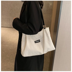 Detail of white corduroy tote bag with black fashion label and wide shoulder straps