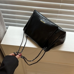 Black leather tote bag with gold logo and metal chain strap on white background