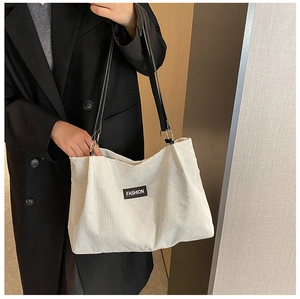 Detail of white corduroy tote bag featuring vertical texture and Fashion logo patch