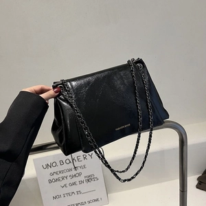 Detail of black glossy leather tote bag featuring golden lettering and dark chain strap