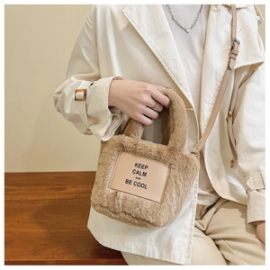 Close-up of fluffy tan faux fur bucket bag with adjustable leather strap on white coat