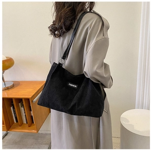 Detail view of the black corduroy tote bag showing the fashion label and metal strap rings