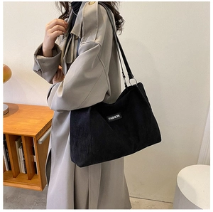 Detail of black corduroy tote bag showing fashion patch and textured fabric on shoulder